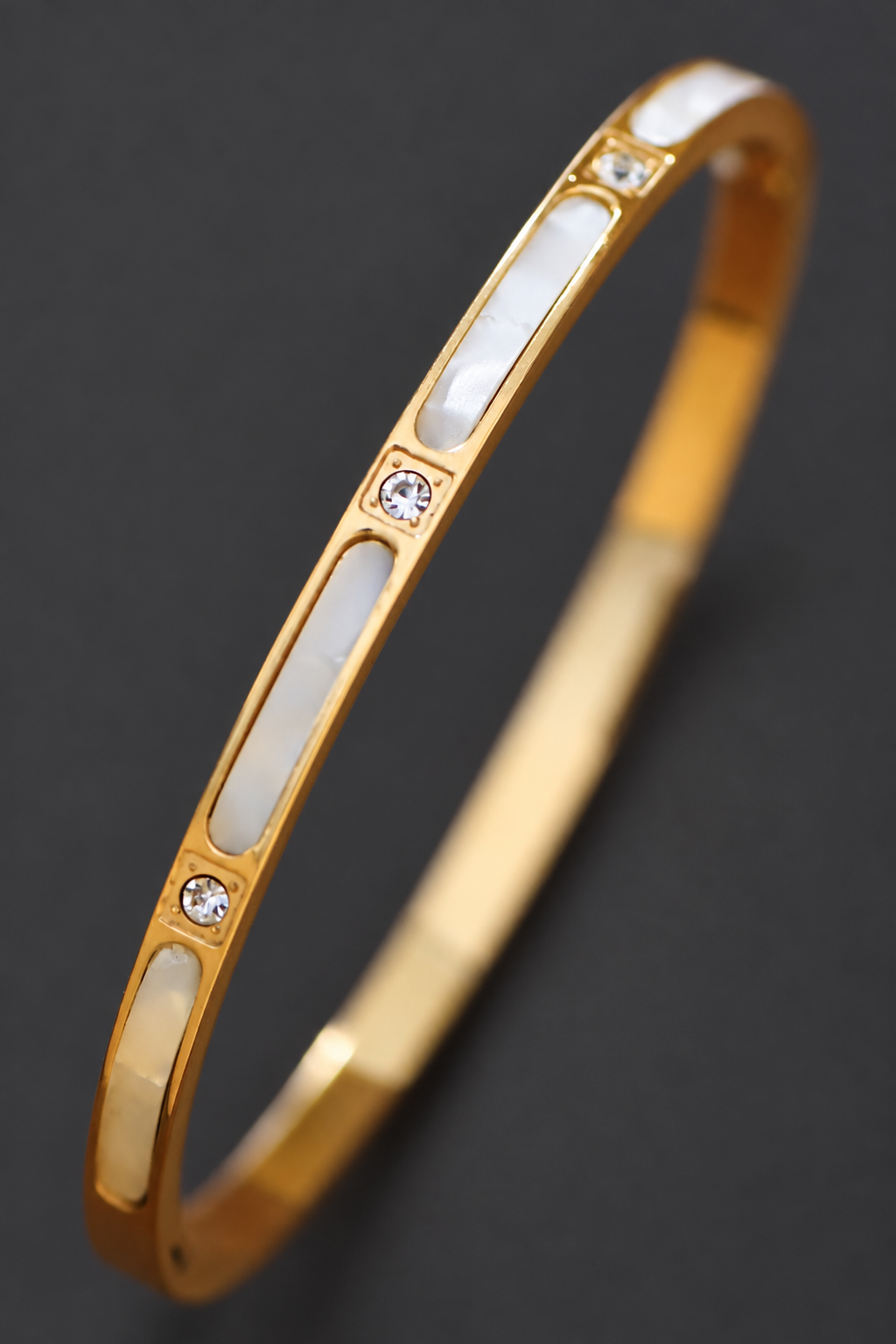 Pulsera rígida ovalada con baño de oro de 18K sobre fondo gris carbón